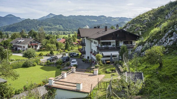 Un grand bâtiment doté d’un toit en pente, entouré d’une végétation luxuriante et avec des montagnes en arrière-plan.