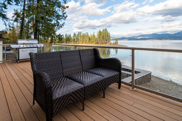 Une terrasse avec un canapé en osier, un barbecue et une vue sur un lac et des montagnes.