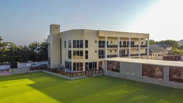 A modern multi-story building with a flat roof, large windows, and a fenced courtyard.