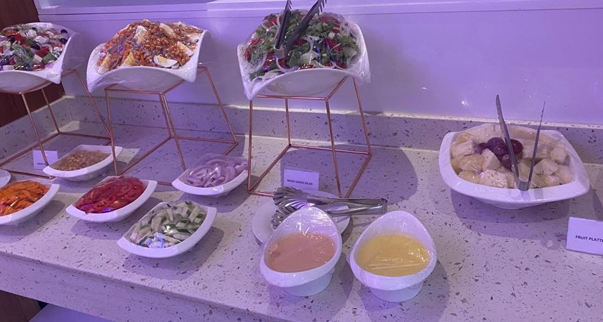 Un bufé con diversos platos, incluyendo ensaladas, frutas y salsas.