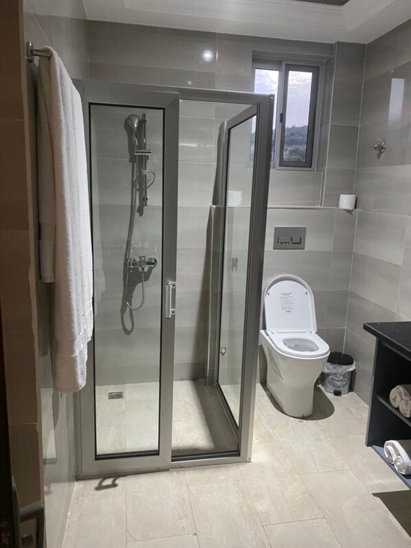 Une salle de bain moderne avec une douche à parois de verre, des toilettes et une petite fenêtre.