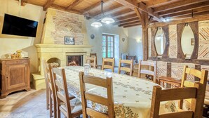 A dining area with a long table, wooden chairs, a fireplace, and a television mounted on the wall. - Quiet Périgord home with jacuzzi & WiFi - 12p (Dordogne)