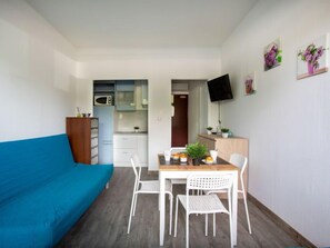 A compact living space with a kitchenette, a dining area with a table and chairs, and a TV mounted on the wall.