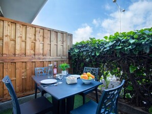 An outdoor dining area with a table set for two, surrounded by a wooden fence and lush greenery.