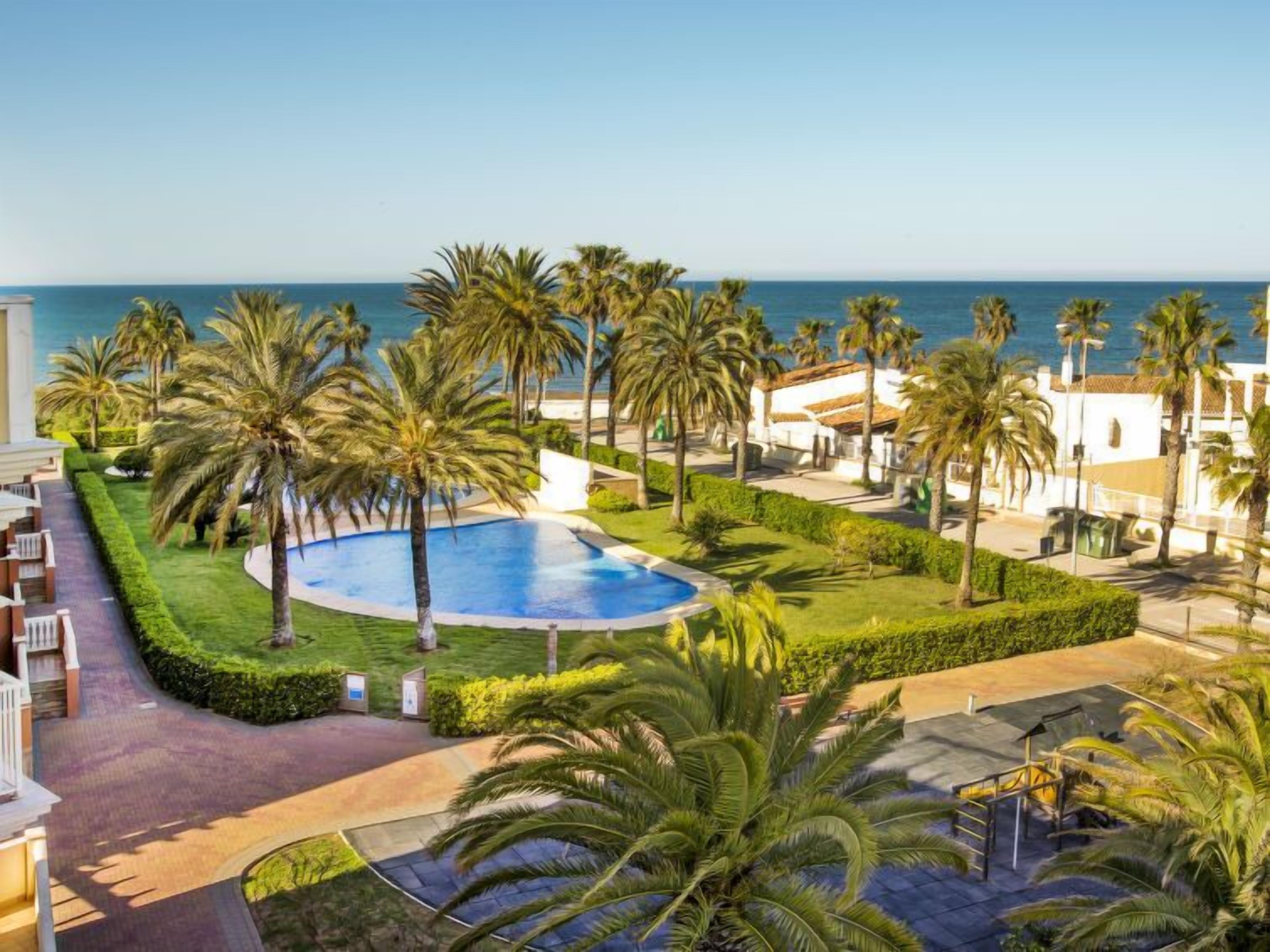 A resort with a swimming pool, palm trees, and a view of the sea.