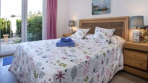 A bedroom with a large bed, a painting of boats, a wooden headboard, and a view of greenery through the window. - Casa Jill by Interhome (Dénia)
