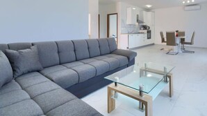 Una sala de estar moderna con un sofá seccional gris, una mesa de centro de vidrio y un comedor con una mesa y sillas blancas.