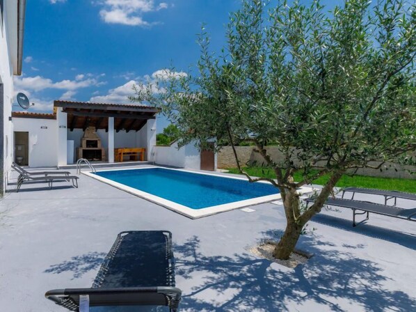 A swimming pool with lounge chairs, a barbecue area, and a tree.