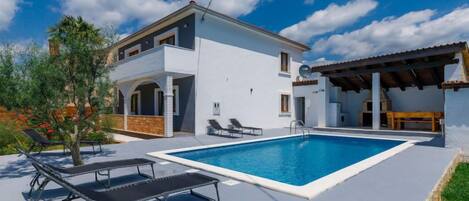 Une maison à deux étages avec une piscine, un espace extérieur aménagé pour se détendre et une terrasse couverte.