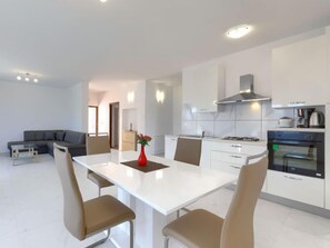 A modern kitchen with white cabinets, a dining table with four chairs, and a built-in oven.