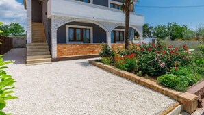 Una casa de dos pisos con un diseño moderno, que cuenta con un balcón y un jardín con flores rojas.
