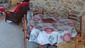 Un coin repas avec un mur en pierre, un tableau, une chaise rouge et une table recouverte d’une nappe à motifs.
