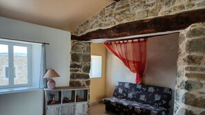 Une pièce chaleureuse avec un mur en pierre, une fenêtre avec des rideaux, un canapé et une petite commode agrémentée d’objets décoratifs.