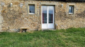 Un bâtiment en pierre avec un toit recouvert de tuiles, une porte centrale et deux petites fenêtres.