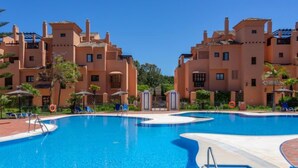Una piscina con agua cristalina y azul, rodeada de una zona de piscina con tumbonas y sombrillas.