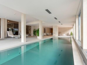 Ein moderner, überdachter Poolbereich mit Liegestühlen und Topfpflanzen.
