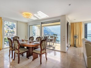 Ein Essbereich mit einem runden Tisch, Stühlen und Blick auf eine gebirgige Landschaft durch große Fenster.