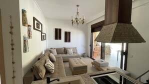 Un salon moderne avec un canapé d’angle, un pouf et une grande fenêtre.