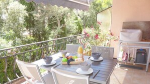 A patio with a table set for breakfast, surrounded by greenery and a barbecue grill. - Le Roumanille by Interhome (Saint Aygulf)