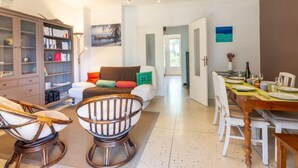A spacious living room with a sofa, a wooden dining table set for four, and a bookshelf. - Le Roumanille by Interhome (Saint Aygulf)