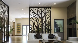 Un vestíbulo moderno con un sofá blanco, una mesa de centro de vidrio y un panel decorativo con motivos vegetales.