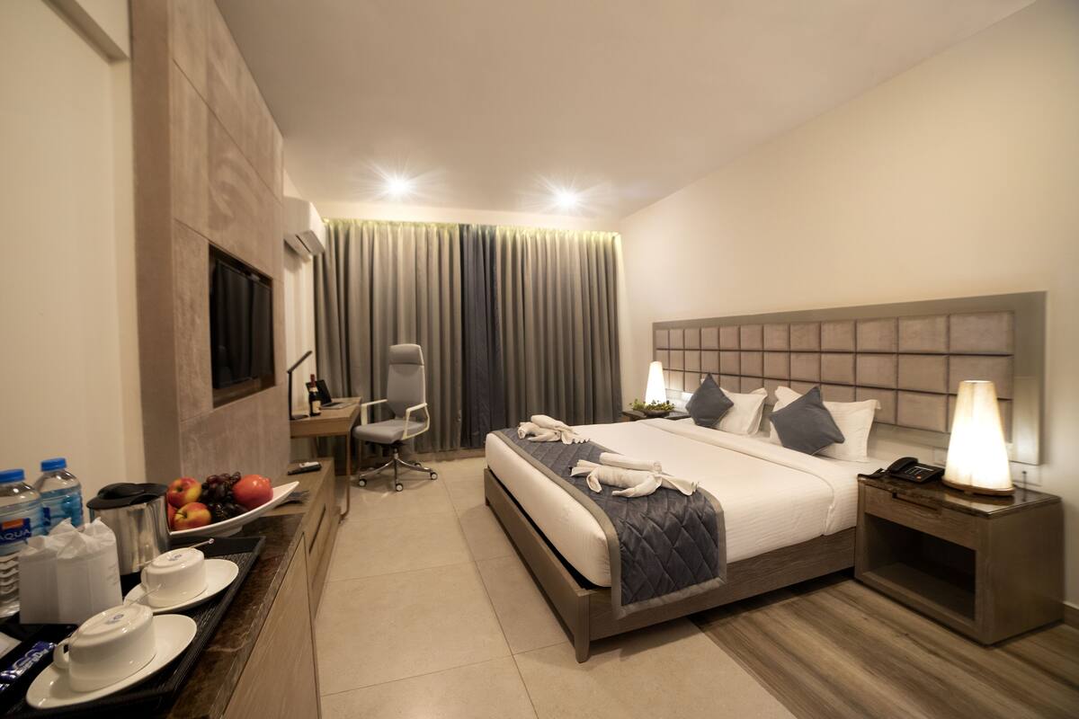 A hotel room with a bed, bedside table, chair, desk, and a TV.