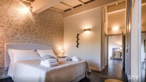 Un dormitorio con una cama grande, una mesita de noche, una lámpara de pared y una puerta que da a otra habitación.