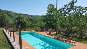 Piscina rectangular con un deck de madera alrededor, equipada con tumbonas y una pequeña mesa.