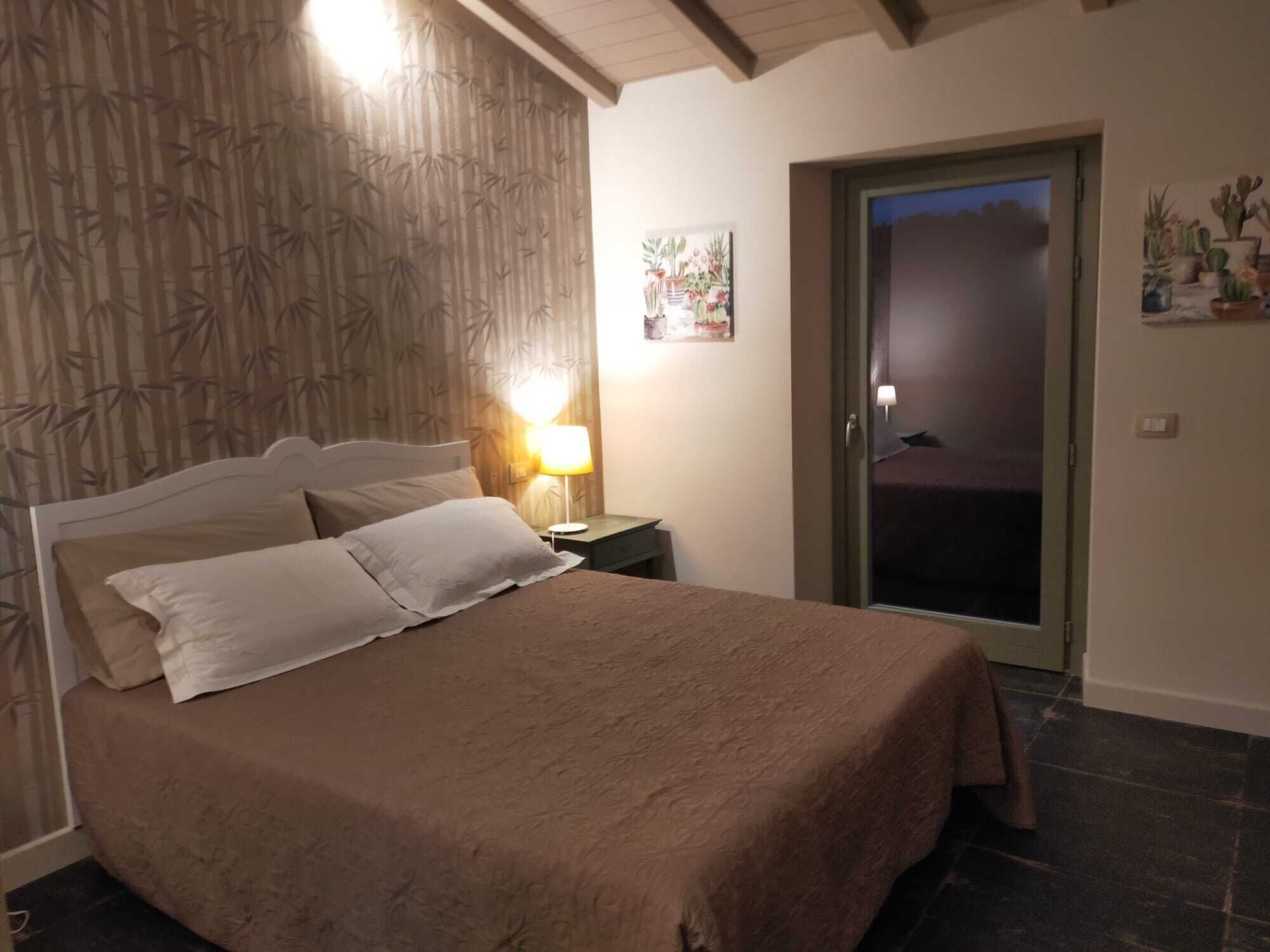 A bedroom with a bed, a nightstand, a lamp, a door, and a wall with a bamboo pattern.