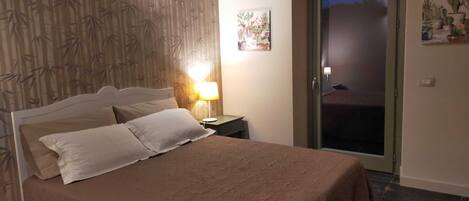 A bedroom with a bed, a nightstand, a lamp, a door, and a wall with a bamboo pattern.