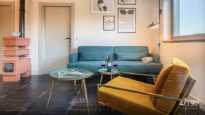 Una sala de estar moderna con un sofá azul turquesa, un sillón amarillo y una mesa de centro de vidrio. Hay obras de arte enmarcadas en la pared y una ventana con vistas.
