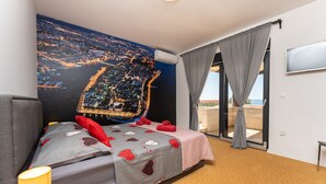 Ett hotellrum med en säng, en tv, ett fönster med gardiner och en väggmålning som föreställer en stadsbild.