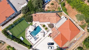 Ett flygbildsbild av en fastighet med en swimmingpool, en tennisbana och en täckt uteplats.
