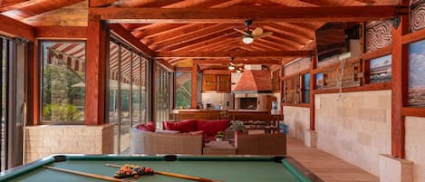 A pool table in a room with wooden beams, large windows, and a fireplace.