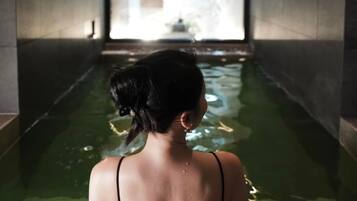 Una persona en una piscina interior estrecha y tenuemente iluminada, con vista a un edificio al fondo.