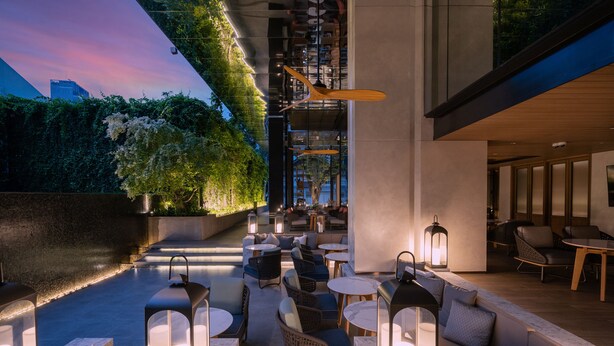 Un espace extérieur aménagé avec des meubles modernes et un éclairage d’ambiance, entouré de verdure et offrant une vue sur le paysage urbain.