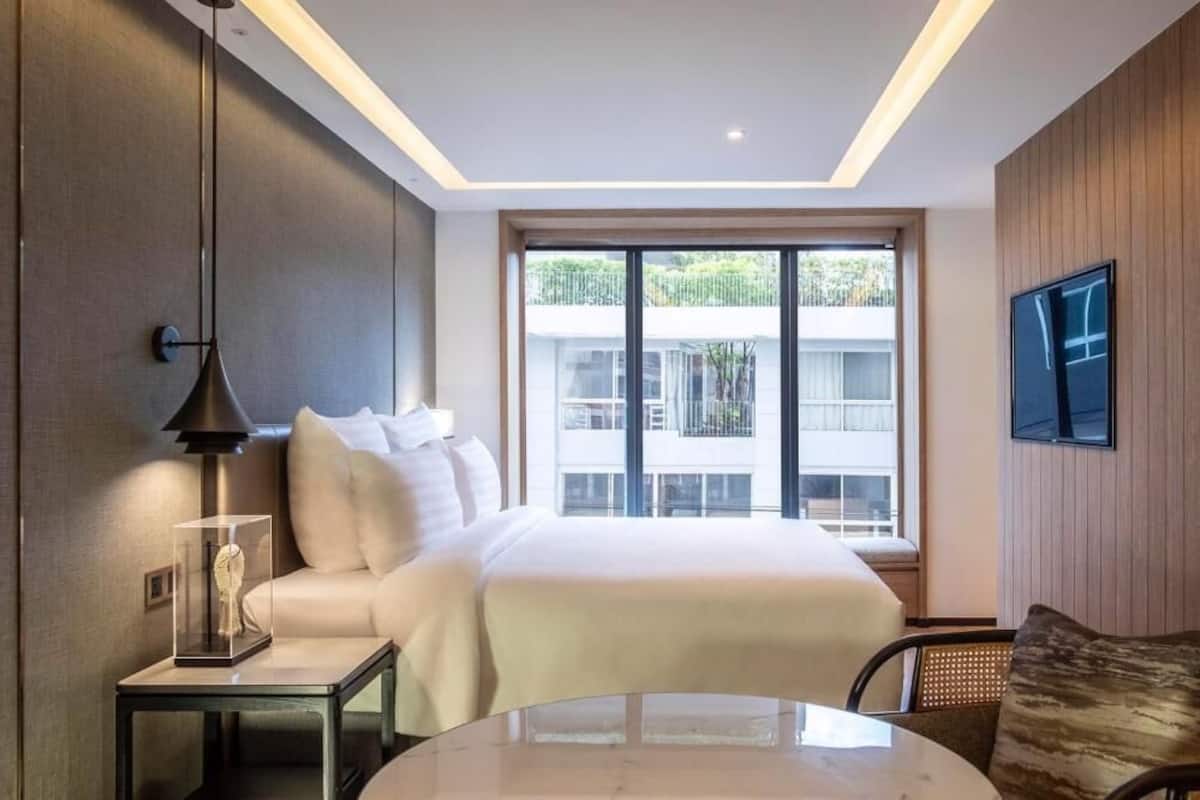 Une chambre d’hôtel moderne avec un grand lit, une table de chevet avec une lampe, une table ronde et un téléviseur fixé au mur.