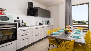 Une cuisine moderne avec des armoires blanches, un four encastré et un coin repas avec des chaises jaunes et une table dressée pour quatre personnes.