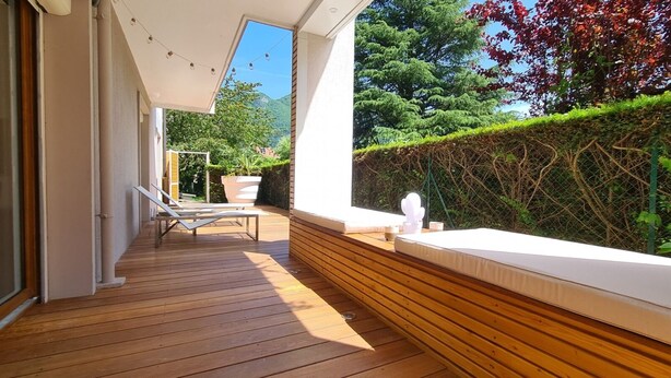 Une terrasse en bois avec un banc blanc doté de coussins et une plante en pot.