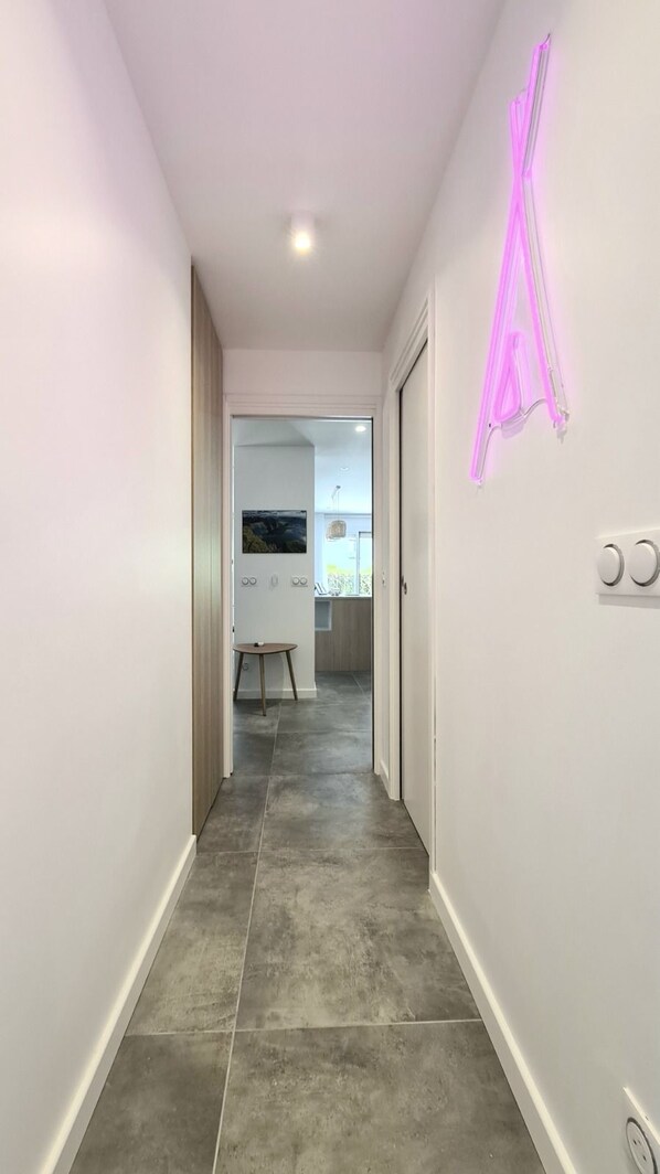 A modern hallway with grey tiled flooring, white walls, and a neon pink sign.