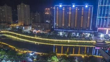 A nighttime view of a cityscape with illuminated high-rise buildings and a river with decorative lighting.