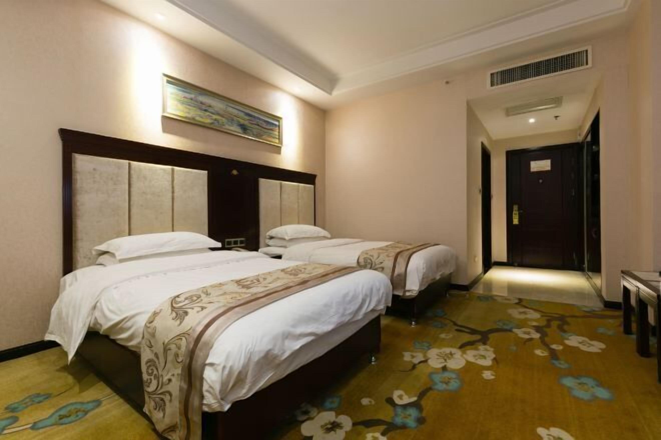 Una habitación de hotel con dos camas, un cuadro grande en la pared y una alfombra estampada con motivos florales.