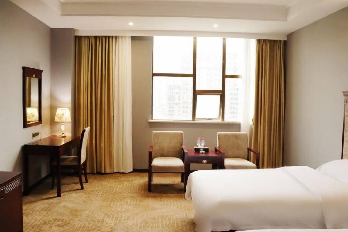 A hotel room with a bed, two chairs, a desk, a lamp, and a window with curtains.