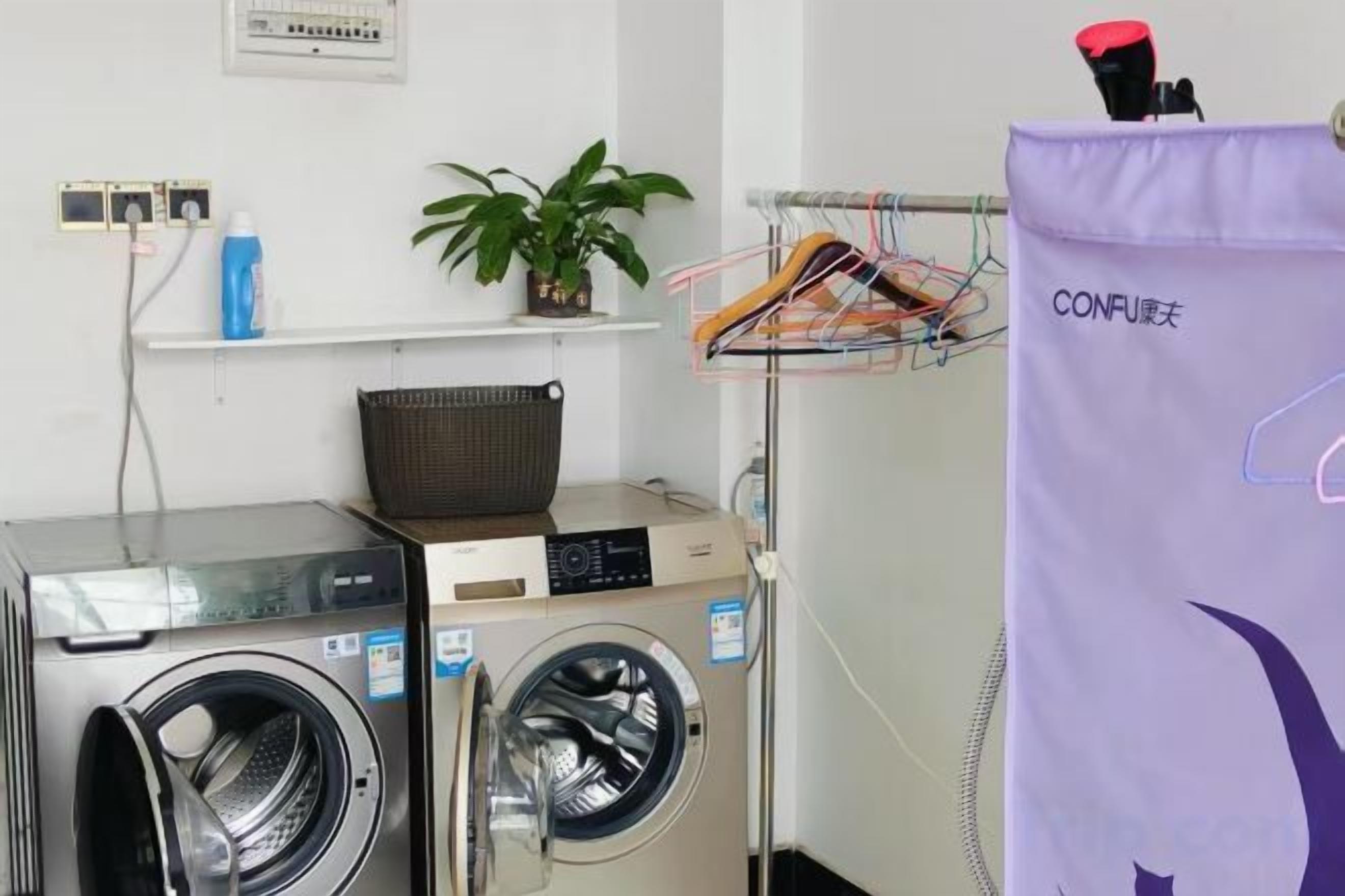 Un espace buanderie comprenant deux machines à laver, un panier, une plante et un sac à linge violet.