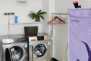 Een wasruimte met twee wasmachines, een mand, een plant en een paarse waszak.