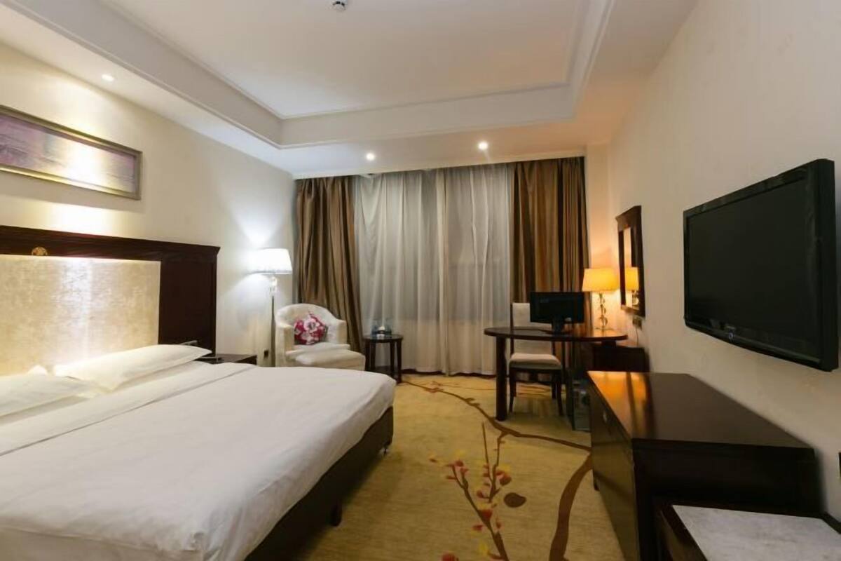 A hotel room with a large bed, a desk, a chair, a TV, and a window with curtains.