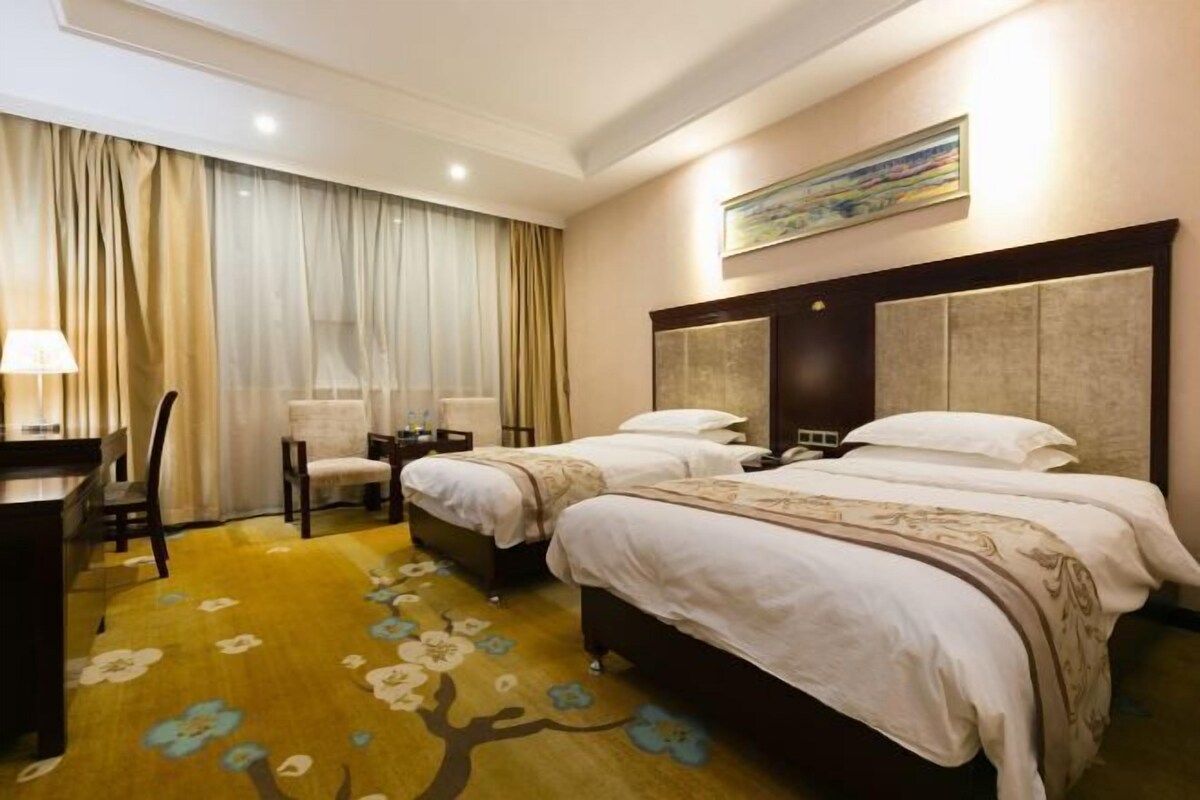 A hotel room with two beds, a desk, and a chair.