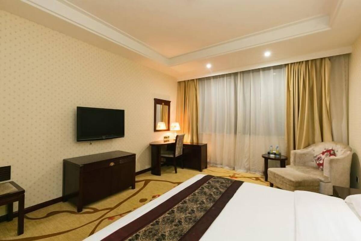A hotel room with a bed, a TV, a desk with a chair, a small table, and a sofa.