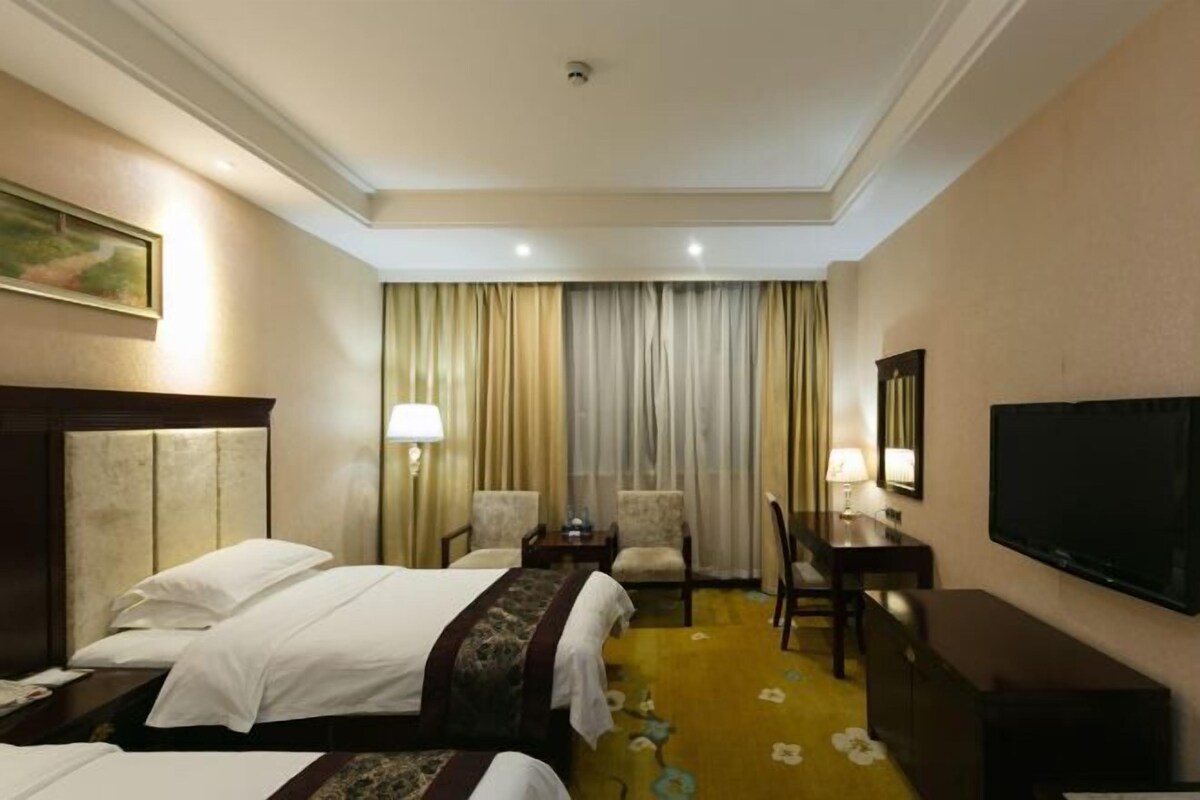A hotel room with two beds, a TV, a desk, and a chair.