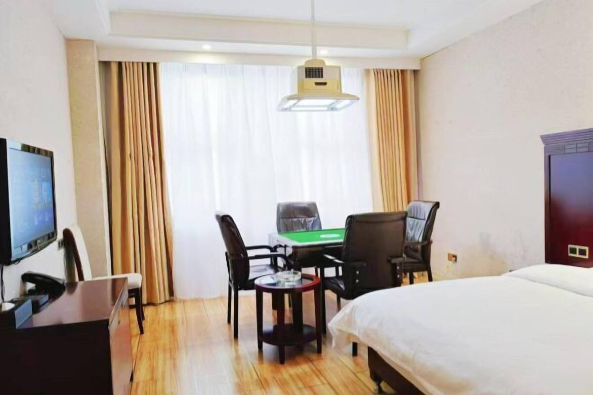 A hotel room with a bed, a desk with a computer, a television, and a view of the outside through large windows.